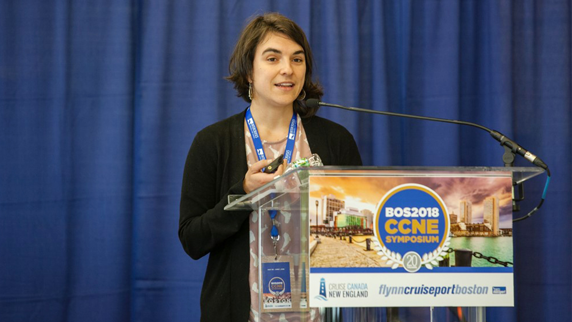 A woman speaks at a conference podium at the Cruise Canada New England Symposium in Boston in 2018